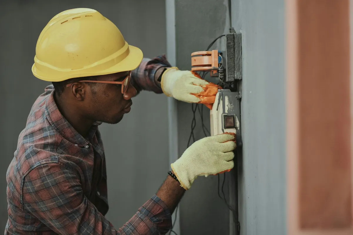 Elektriker mit Schutzhelm bei der Montage einer Installation (Symbolbild)